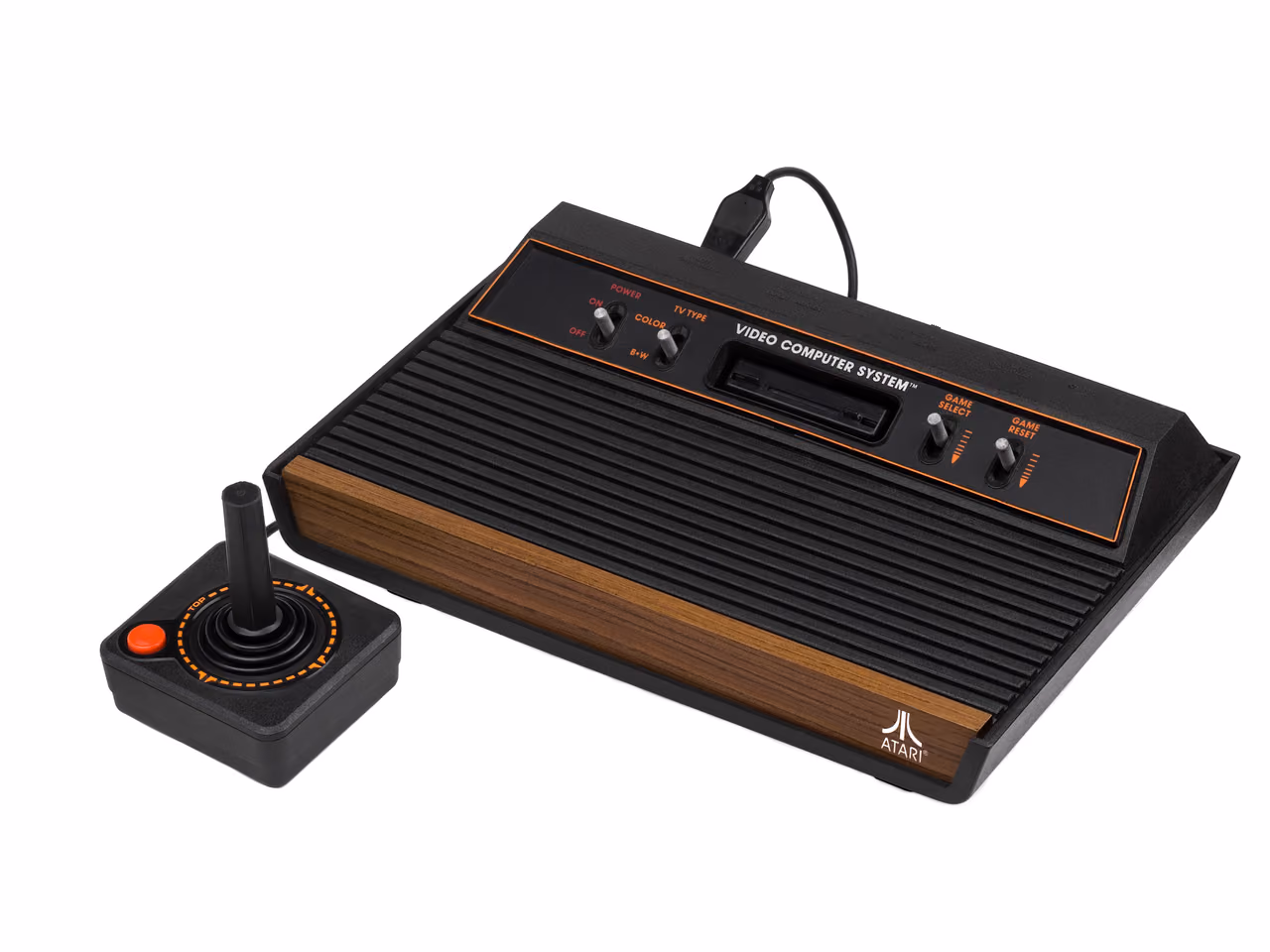 A black Atari 2600 with a wood-grain front panel photographed against white, six silver switches along its top edge and a cartridge slot behind them, with a single-button joystick standing in front of it.
