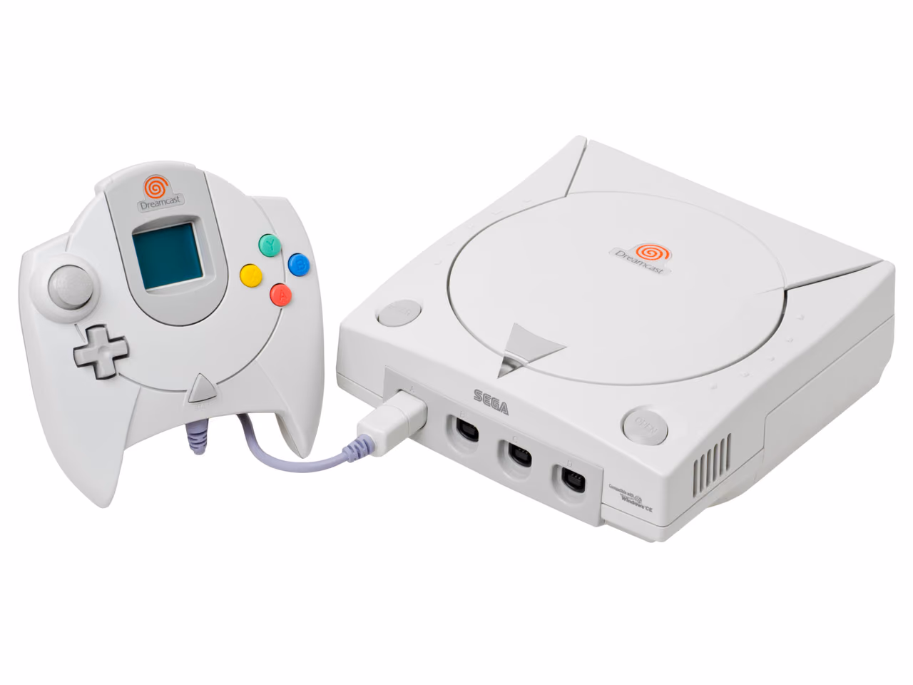 A white Sega Dreamcast photographed against white, a circular disc lid marked with the orange Dreamcast spiral set into its top, with the controller standing to the left, a small screen in the middle of it.