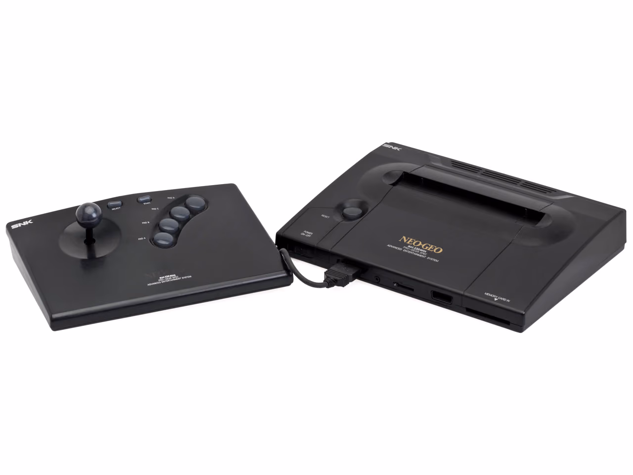 A black SNK Neo Geo AES photographed against white, with an arcade-style joystick controller of nearly the same size standing to its left and connected to it by a thick cable.