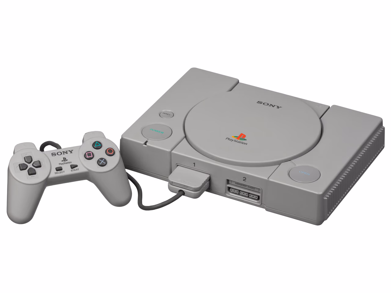 A gray Sony PlayStation photographed against white, its round disc lid closed on the top of the case, with the original controller lying to its left and a memory card in the second front slot.